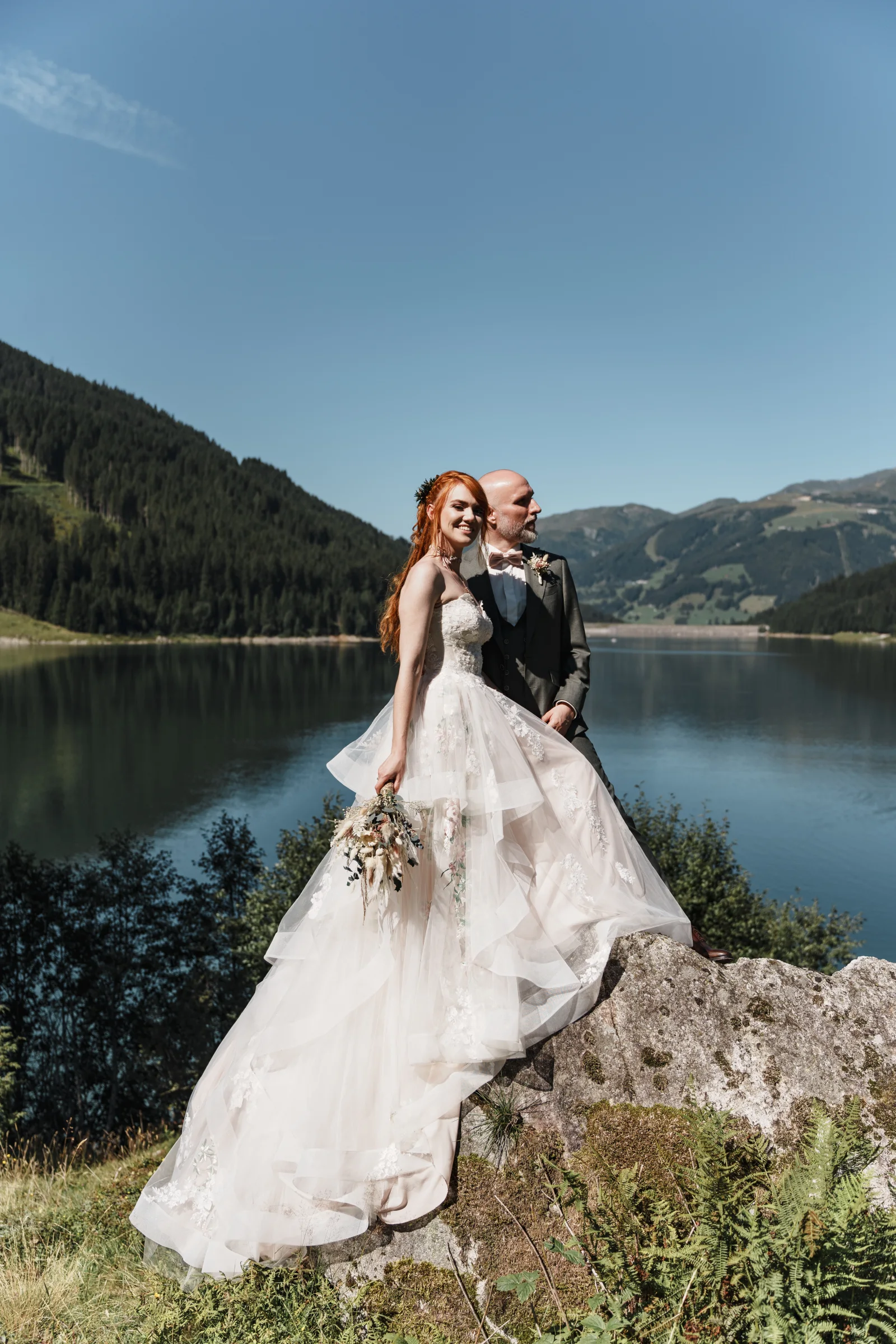 Brautpaar steht auf einem Felsen am See