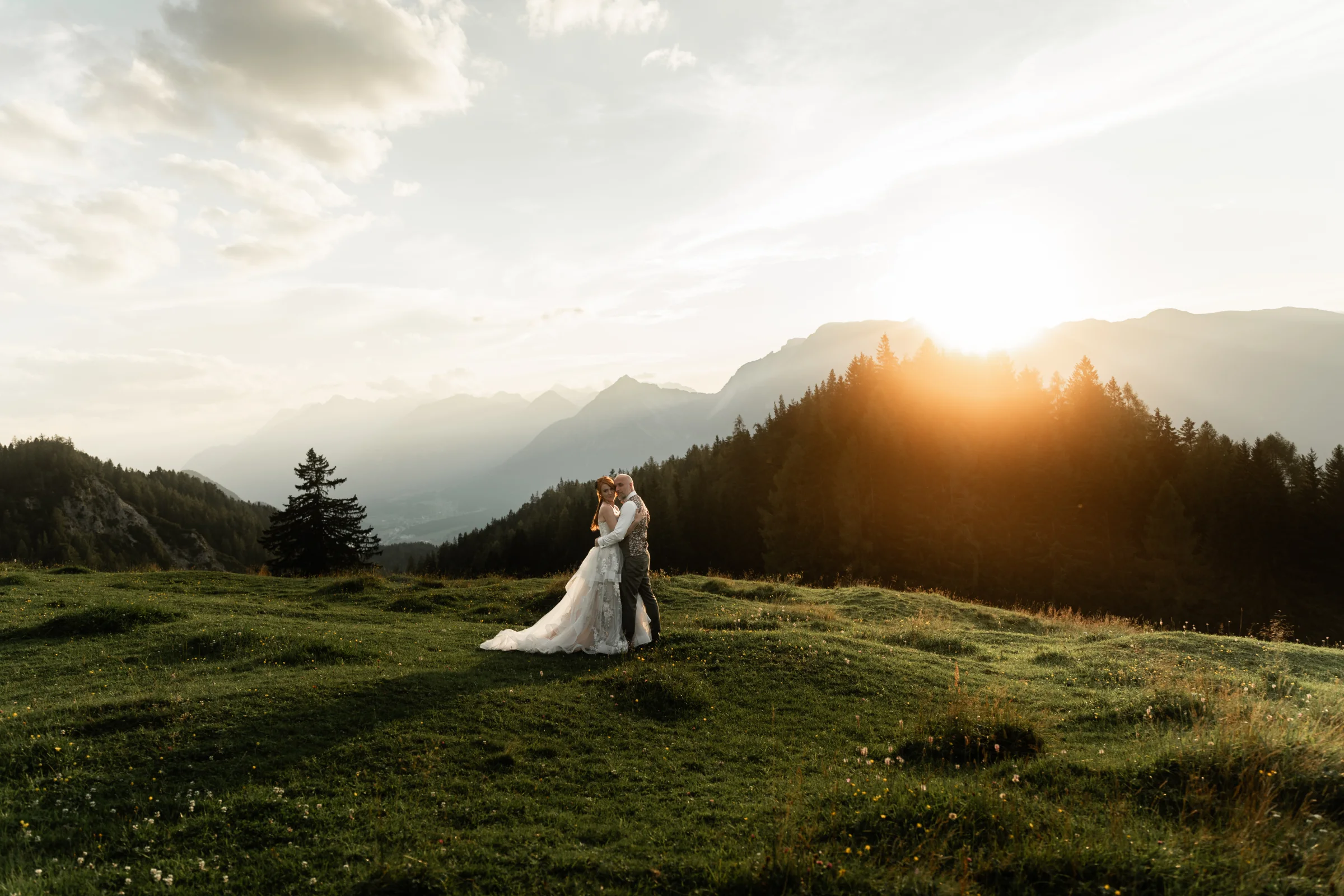 Brautpaar steht im Sonnenuntergang auf einem Berg in den Alpen